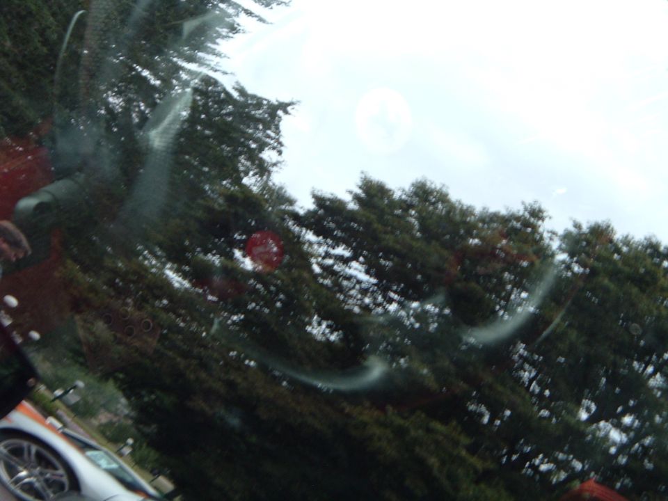Silver car side view, partially obscured by windshield glare and trees