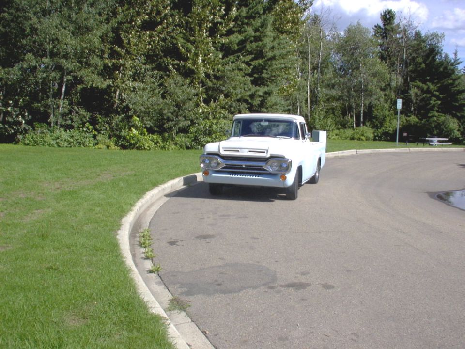 White vintage pickup truck front view on curved road by grass and trees