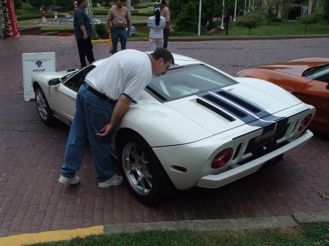 1999 Mercury Grand Marquis - Man inspects the engine of a white Ford GT with blue racing stripes parked on brick pavement.