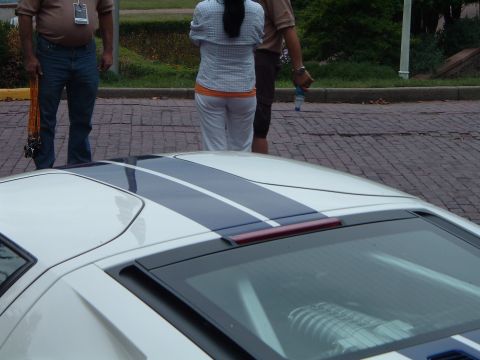 1999 Mercury Grand Marquis - A white sports car with racing stripes is parked on a brick surface, with several people standing nearby.