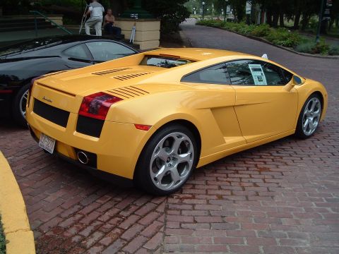 1999 Mercury Grand Marquis - A yellow Lamborghini Gallardo is parked on a brick road next to a black car.