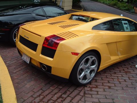 1999 Mercury Grand Marquis - A yellow Lamborghini Gallardo is parked on a brick surface, with a black car visible behind it.