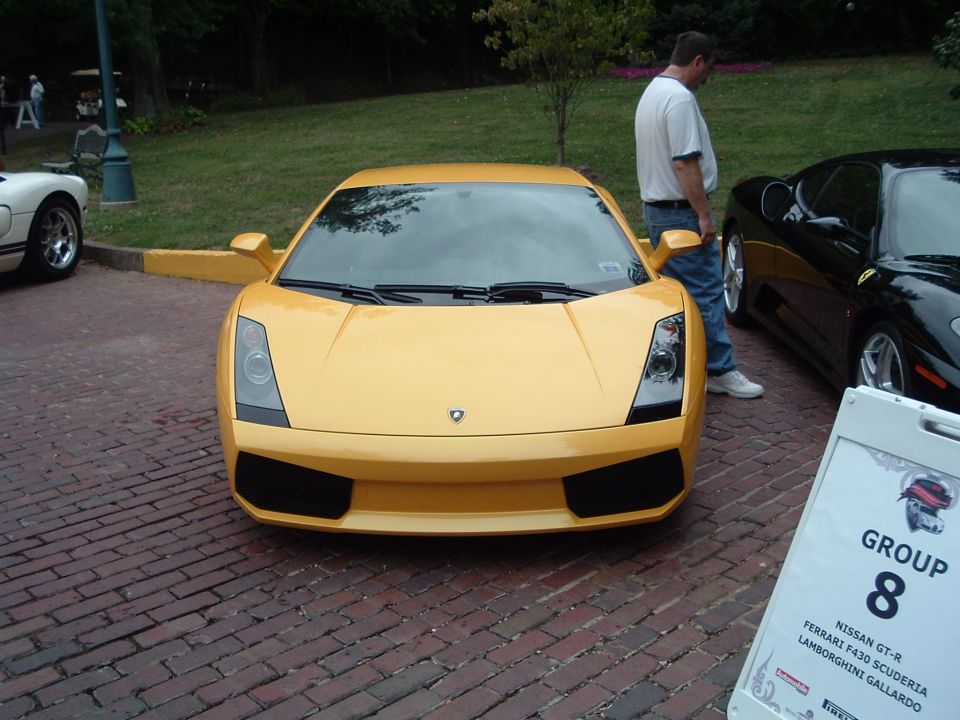 Yellow Lamborghini Gallardo parked on brick road, black Ferrari F430 next to it