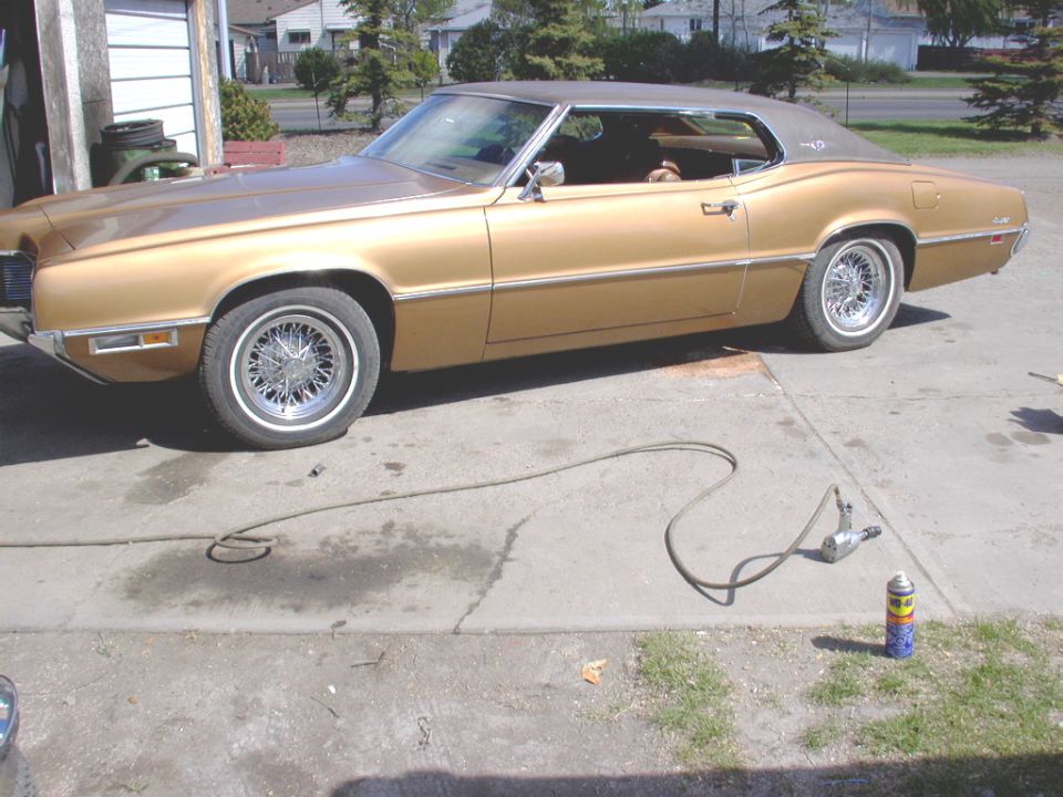 Gold two-door coupe with tan vinyl roof and wire wheels parked in a driveway
