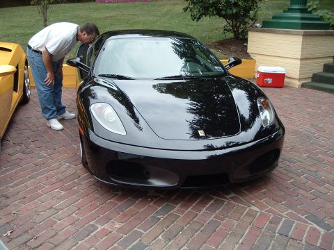 1999 Mercury Grand Marquis - A man inspects a black Ferrari F430 parked on a brick surface next to a yellow Lamborghini.