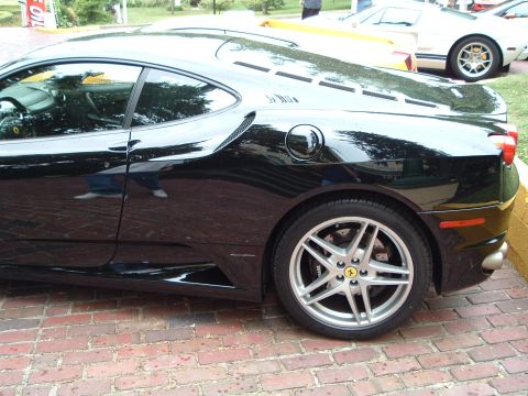 1999 Mercury Grand Marquis - Black Ferrari F430 sports car parked on brick pavement, with another vehicle in the background.