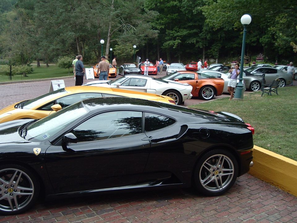 Black sports car parked next to a yellow sports car, with other cars and people in the background