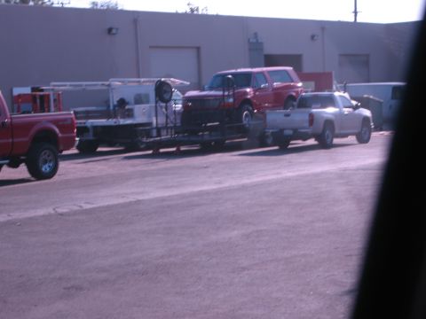 1986 Ford Bronco - A red Ford Bronco is loaded onto a trailer, towed by a silver pickup truck.