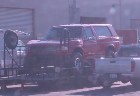 1986 Ford Bronco - A red Ford Bronco is transported on a trailer, showing its lifted suspension and off-road tires.
