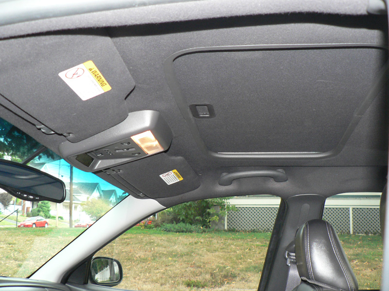 Black headliner with sunroof shade, overhead console and visor warning label inside a car