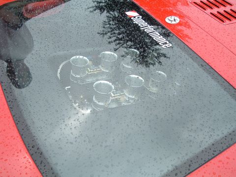 1999 Mercury Grand Marquis - A red car hood displays a six-cylinder intake manifold under a panel covered in water droplets.