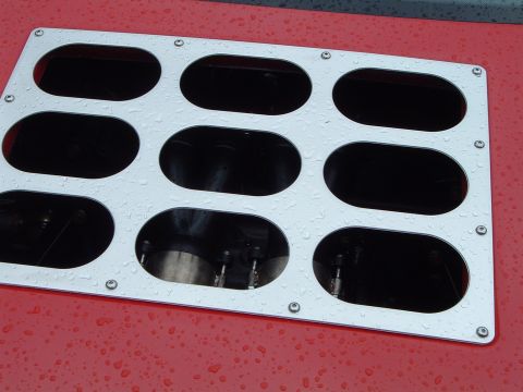 1999 Mercury Grand Marquis - Close-up of a silver engine intake manifold cover with multiple openings, wet from rain.