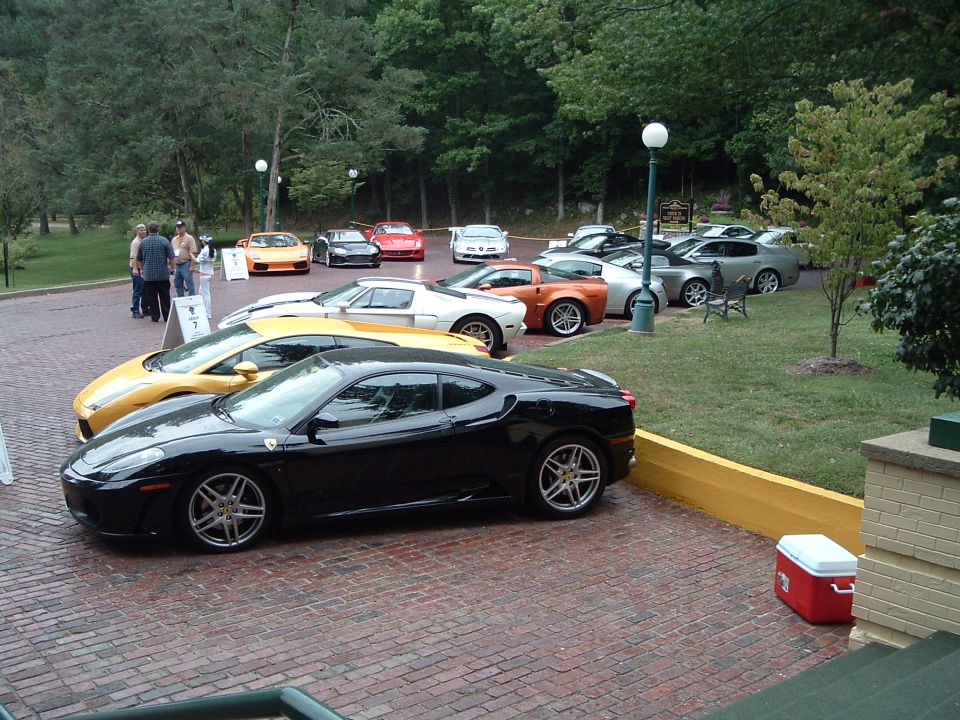 Black Ferrari coupe parked on brick driveway with yellow Ferrari and other sports cars