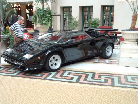 1999 Mercury Grand Marquis - A man stands next to a black sports car with a distinctive angular design and scissor doors.