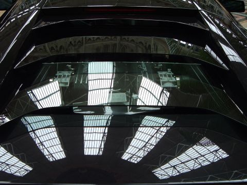 1999 Mercury Grand Marquis - Reflections on the rear engine cover of a black sports car, showing a glass roof structure and website text.
