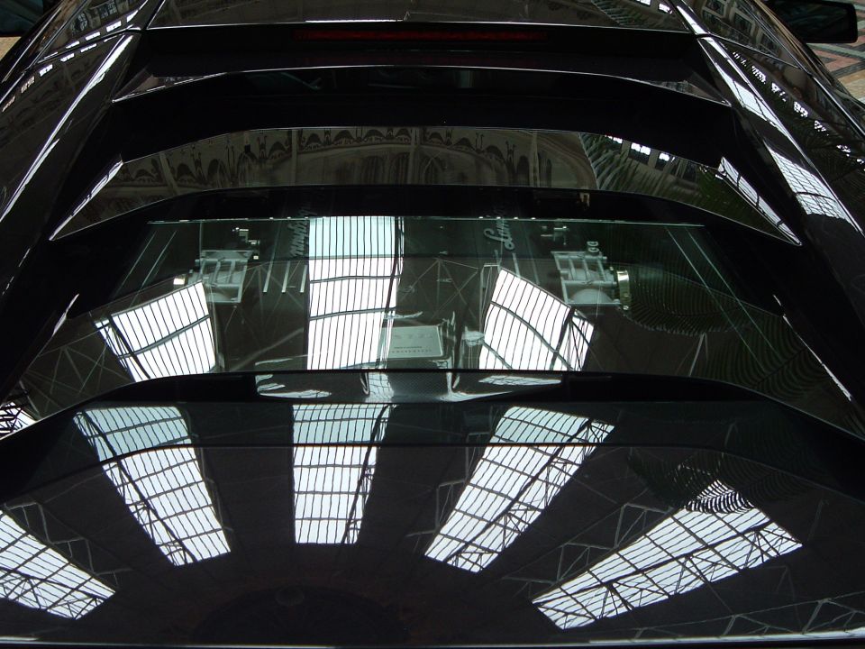 Skylights and roof trusses reflected in the mirror-finish black hood and windshield of a car