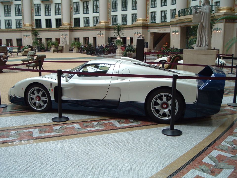 White and blue Maserati MC12 supercar displayed behind ropes in a hotel atrium