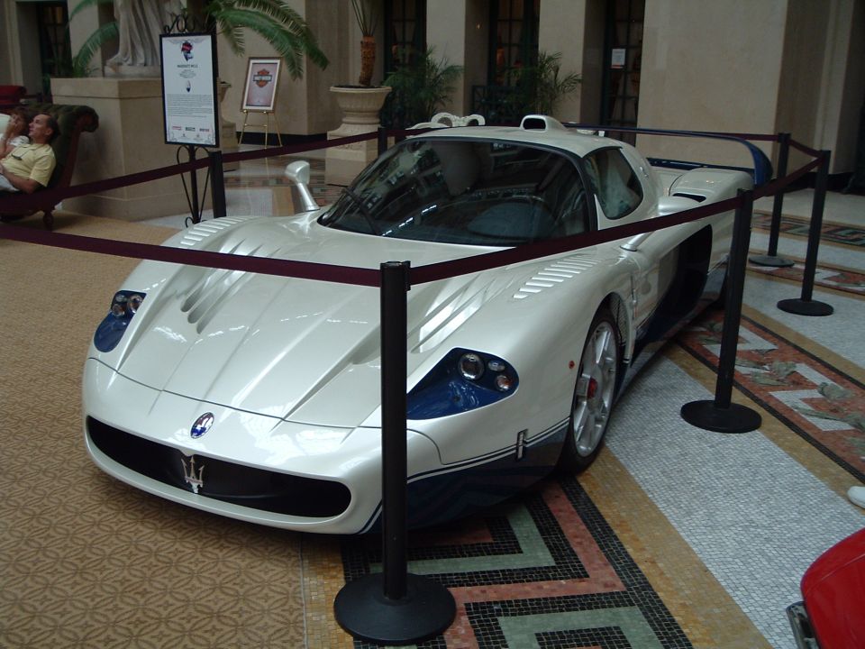 White Maserati MC12 supercar on display behind ropes in a marble lobby, front three-quarter view