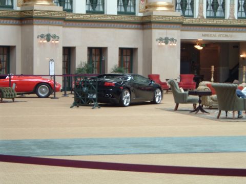 1999 Mercury Grand Marquis - A black sports car is displayed indoors, positioned behind a red convertible and near seating areas.