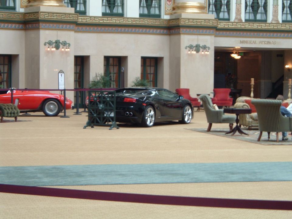 Black Lamborghini Gallardo and red vintage roadster displayed in hotel atrium lobby