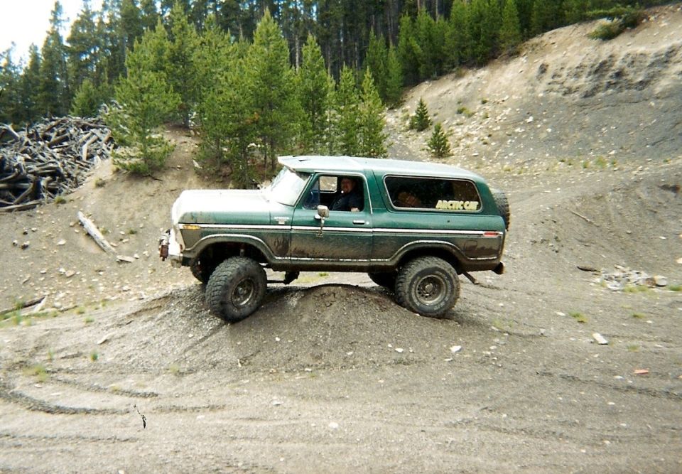 Green and white Ford Bronco climbing a dirt embankment