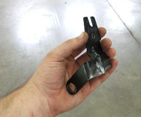 1985 Ford LTD Crown Victoria - A person holds a metal bracket, likely a car part, against a concrete floor.