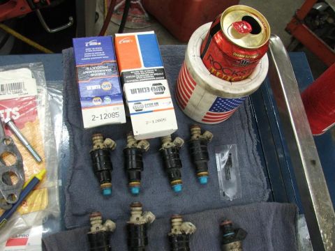 1985 Ford LTD Crown Victoria - Several fuel injectors and NAPA parts boxes are laid out on a blue cloth next to a drink koozie.