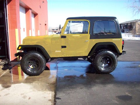 1985 Ford Bronco - A yellow Jeep CJ is parked outside a building with a black hardtop and off-road tires.