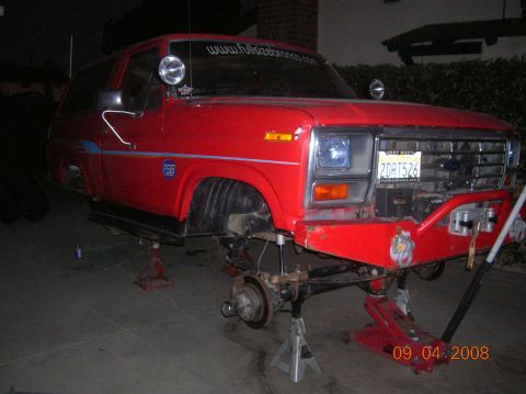 1985 Ford Bronco - Front view of a red 1985 Ford Bronco undergoing maintenance, lifted on jack stands.