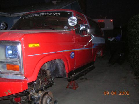 1985 Ford Bronco - A red Ford Bronco is shown with its front end disassembled while on jack stands.