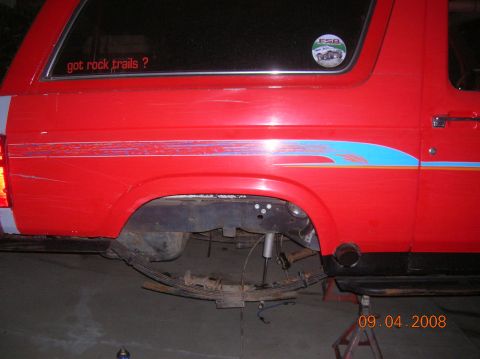 1985 Ford Bronco - The rear suspension of a red Ford Bronco is exposed, showing leaf springs and shock absorbers.
