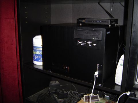 1989 Ford Bronco - A black computer tower is shown on a shelf, accompanied by a bottle of monitor wipes and various cables.