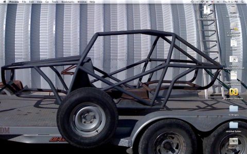1994 Ford Bronco - Custom tube chassis race car frame on a trailer, viewed from the side against a corrugated metal wall.