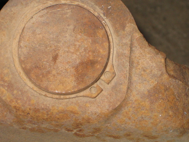 Rusted metal part with circular indentation and two small bolt holes