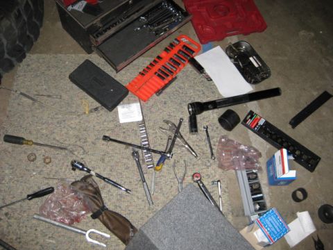 1995 Ford Bronco - Various tools and what appear to be ball joint components are spread across the garage floor, suggesting recent mechanical work.