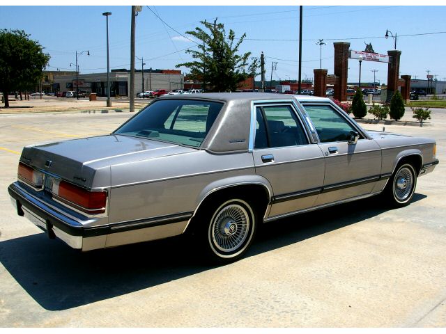 Silver/gray four-door sedan, rear 3/4 view with wire wheels in a parking lot