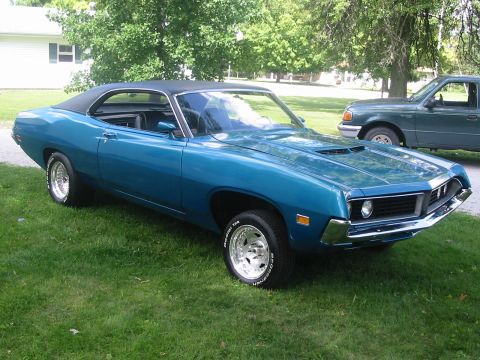 1970 Ford Fairlane - A blue 1970 Ford Fairlane coupe with a black vinyl roof sits on a grassy lawn next to a green pickup truck.