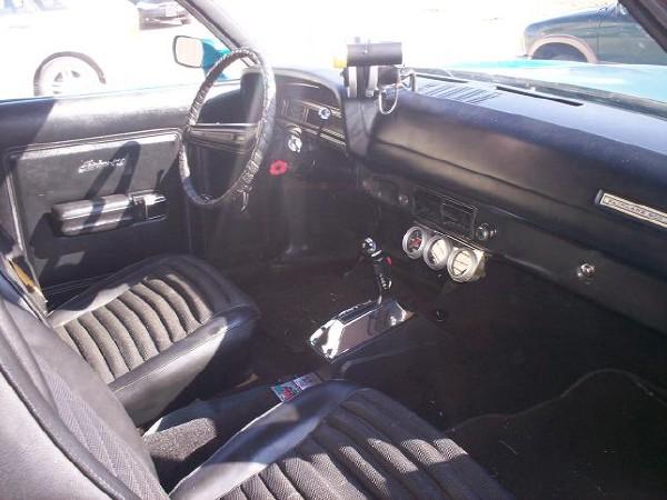 Black interior of a 1970 Ford Fairlane showing ribbed seats, dashboard with gauges, and steering wheel