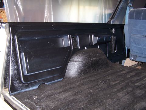 1986 Ford Bronco - Freshly black-painted rear inner bed and wheel-tub panel of a truck/SUV, with bedliner-textured floor and blue exterior body edge visible.