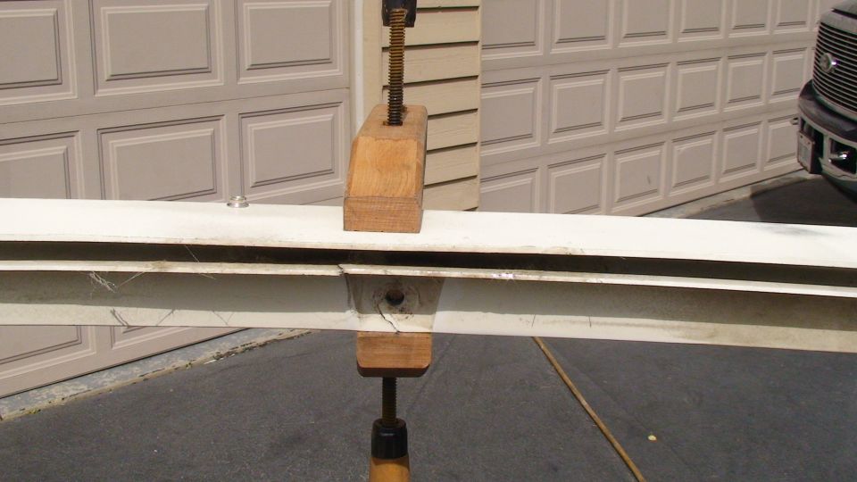 White metal beam clamped with wood blocks, with a garage door and part of a dark truck visible