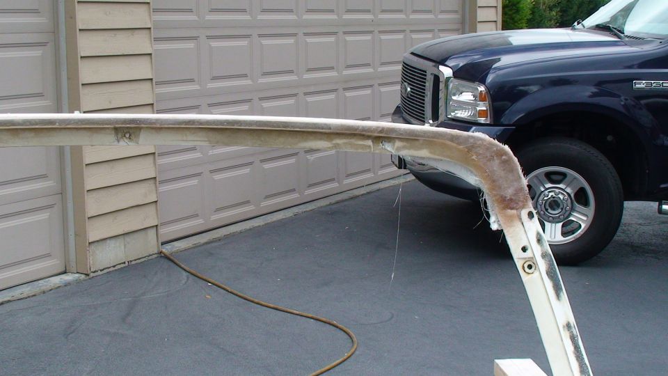 Damaged fiberglass body panel in front of a dark blue Ford F-350 and a garage.