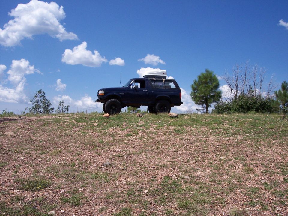 Lifted dark blue Ford Bronco with roof cargo box parked on a rocky ridge