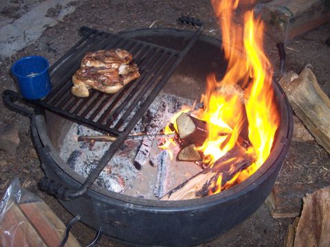 1996 Ford Bronco - A chicken is being grilled over an open fire pit. A blue enamel mug sits on the edge of the grill.