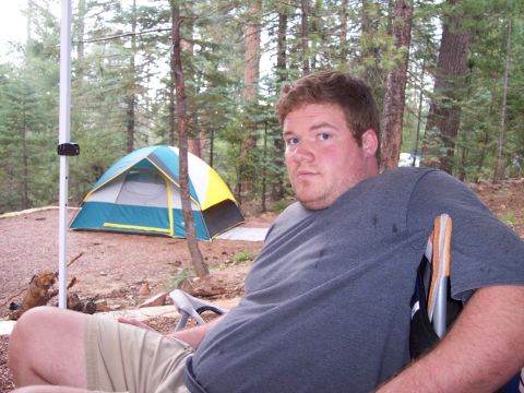 1996 Ford Bronco - A man sits in a camping chair in a wooded area with a tent set up behind him.