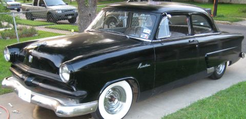 1953 Ford Mainline - Black two-door sedan badged 'Monterey' with chrome bumpers and wide whitewall tires parked on a residential lawn.