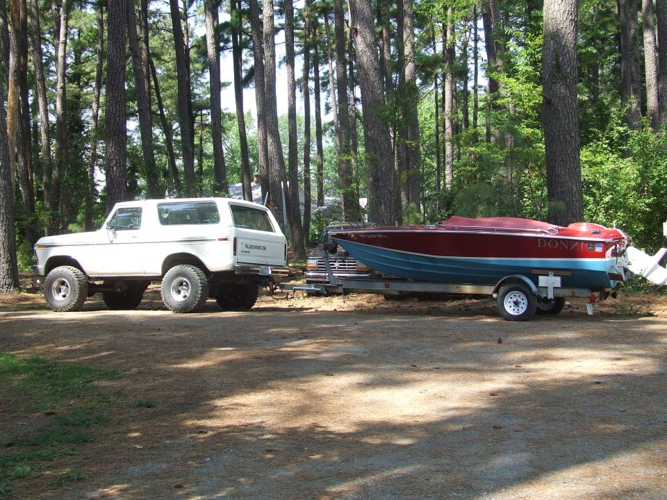 White Ford Bronco parked next to a red and blue Donzi boat on a trailer.