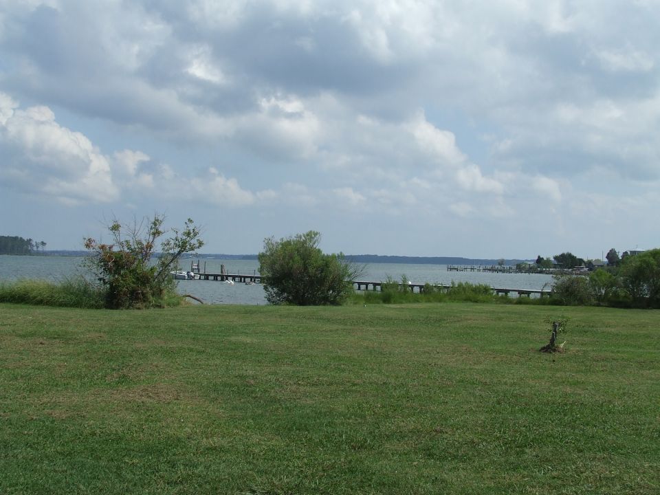 Grassy lawn leading to a water scene with piers and boats under a cloudy sky.