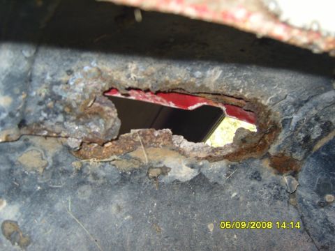 1989 Ford Bronco - This is a close-up view of heavily rusted metal, likely a vehicle frame or body panel, with a large hole revealing a red surface underneath…