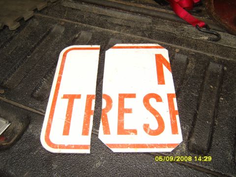 1989 Ford Bronco - Two pieces cut from a white and orange 'NO TRESPASSING' aluminum sign, laid on the ribbed rubber mat of a pickup bed with the corners trimm…