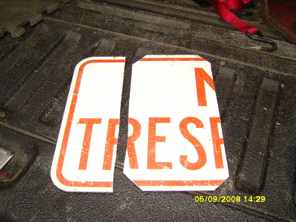 Two cut pieces of a no-trespassing aluminum sign lying in a pickup bed
